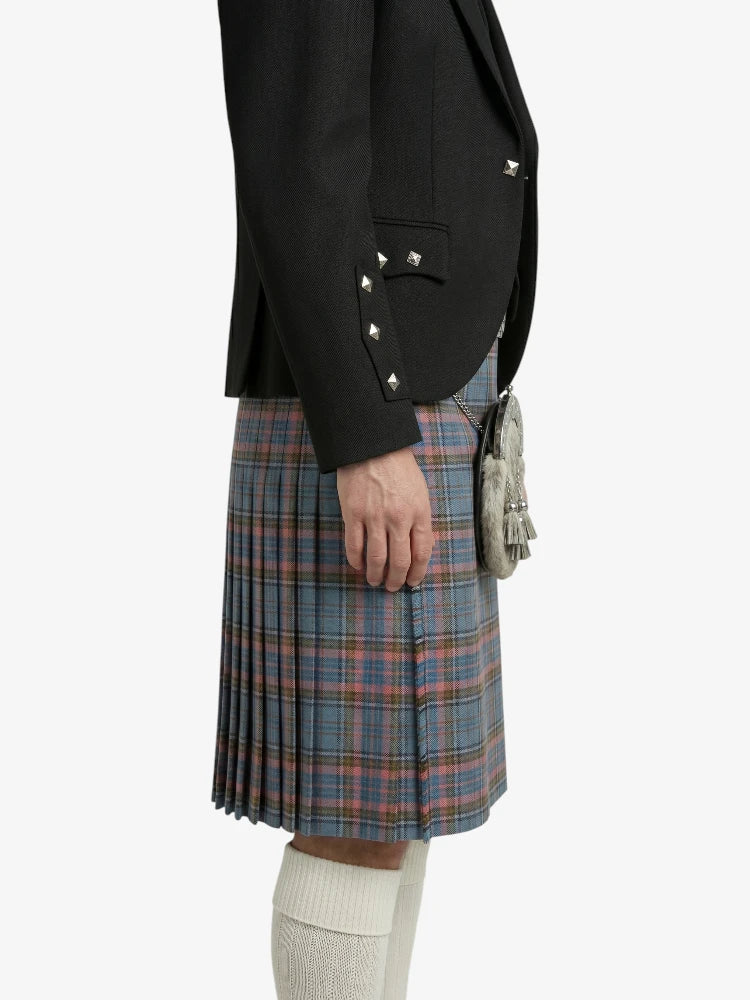 Person wearing a black blazer with studded details and a plaid kilt on a white background