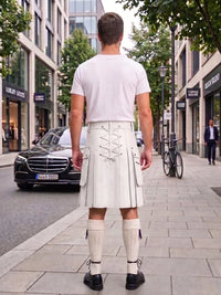 A man viewed from behind wearing a white t-shirt and a cream-colored kilt with lace-up detailing, standing on a city sidewalk.