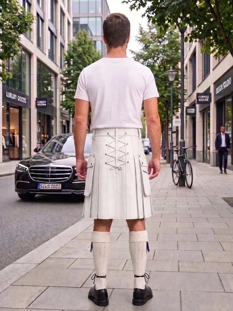 A man viewed from behind wearing a white t-shirt and a cream-colored kilt with lace-up detailing, standing on a city sidewalk.
