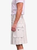 A side view of a person wearing a light beige pleated kilt with flap pockets and silver snap buttons, paired with a white t-shirt, against a plain white background.