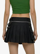 Person wearing a green crop top and black pleated skirt with buckles on a white background
