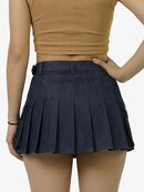 Person wearing a navy pleated skirt and beige top on a white background