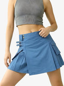 Person wearing a blue pleated skirt and gray crop top on a light gray background