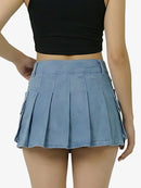 Person wearing a black crop top and blue pleated skirt on a plain background