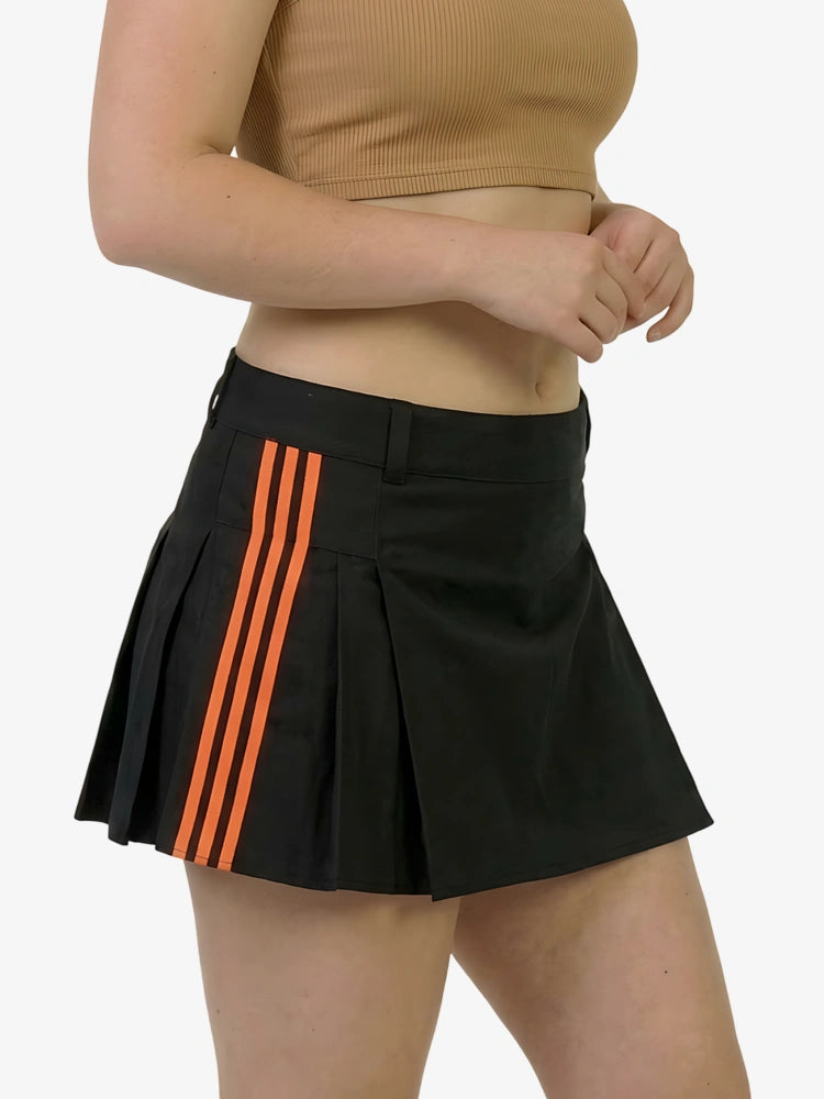 Black pleated skirt with orange stripes worn by a person on a white background