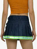 Person wearing a navy pleated skirt with reflective stripes and an orange top on a white background